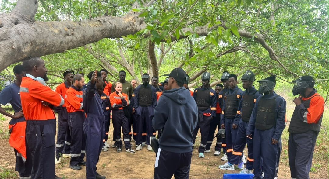 Large corporate group gathered under a tree for the safety briefing before a team building session
